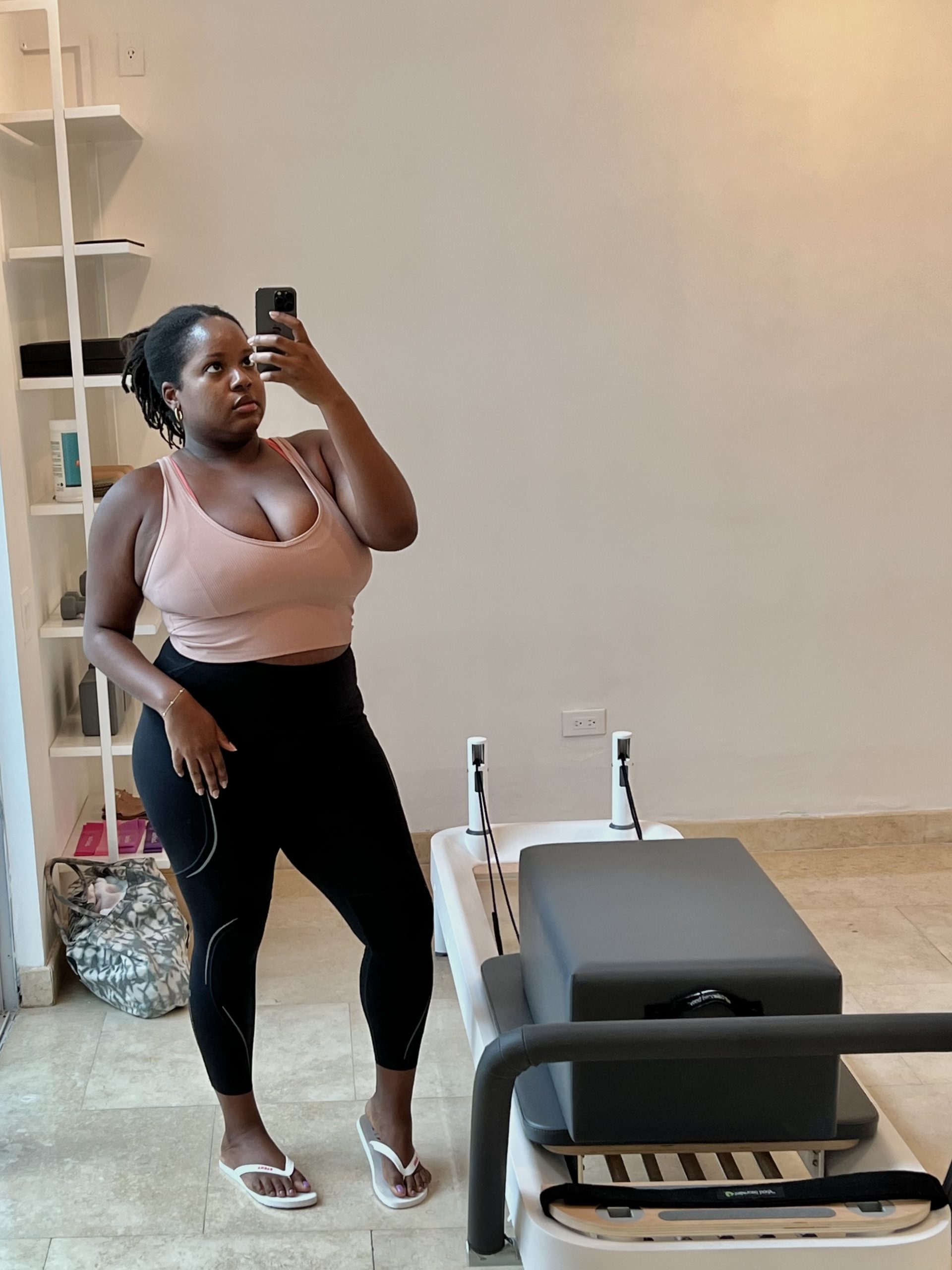 Black woman with curvy fit body in private Pilates studio standing next to reformer